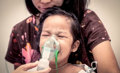 Woman holding inhaler mask to child's face. Image, Adobe.